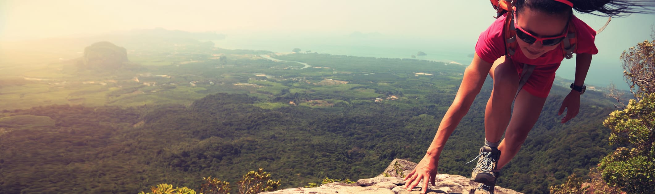 A young asian woman hiker climbing rock on mountain peak cliff